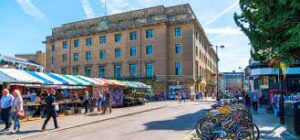 An exterior view of Allia Future Business Centre, Cambridge Guildhall, Market Square, Cambridge, CB2 3QJ with a market in the foreground